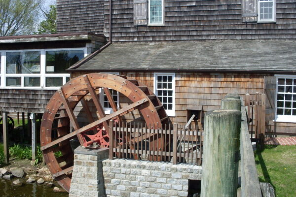 Rustic water wheel attached to a wooden building near a stone wall.